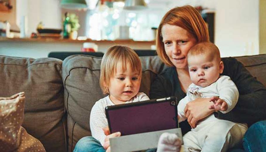 Una madre con dos bebés viendo la tablet en el sofá