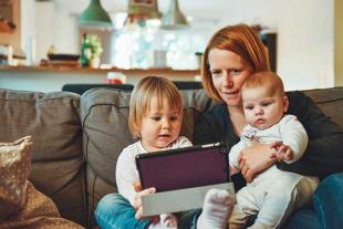 A mother with two babies looking at the tablet on the couch